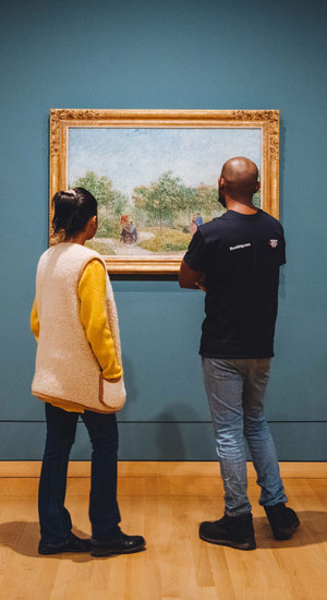 Twee bezoekers kijken naar het schilderij Tuin met geliefden: Square Saint-Pierre van Vincent van Gogh. Foto: JD Photography