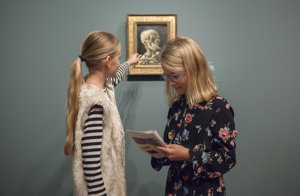 Twee meisjes in het museum bij het schilderij 'Kop van een skelet met brandende sigaret'